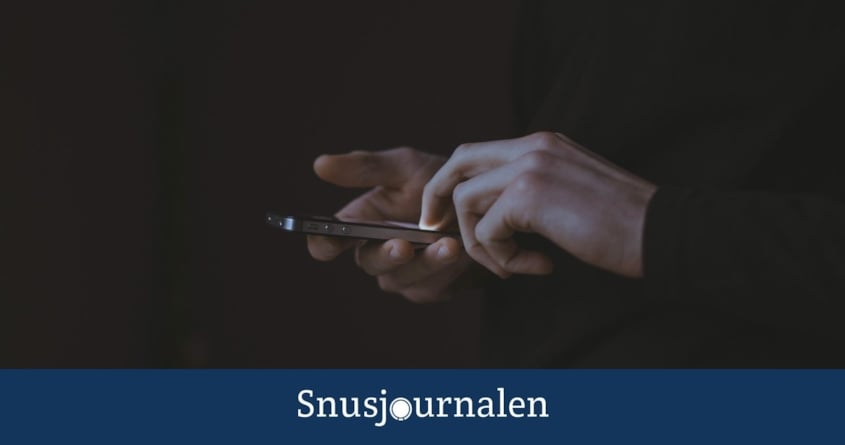Hand som skriver med mobilen med mörk bakgrund - snus från svarta marknaden