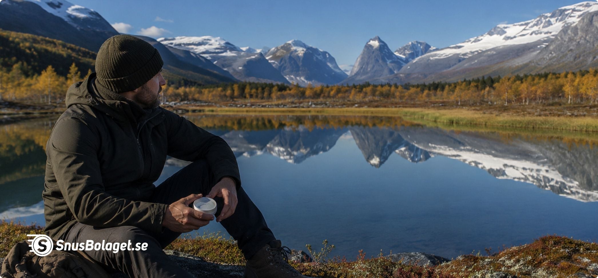 En man sitter vid en sjö i norrbotten med en snusdosa i handen.